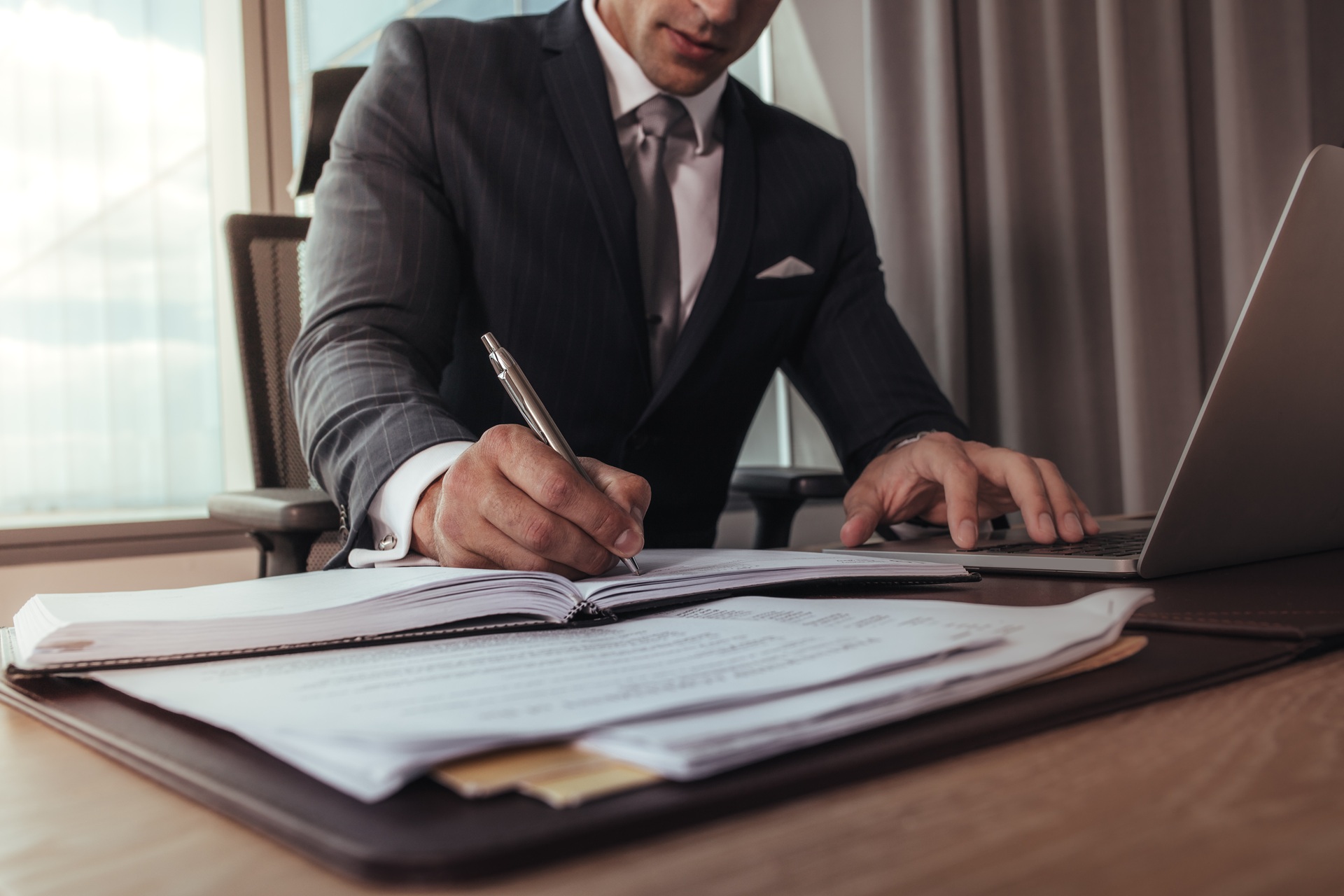 An attorney sits at a desk writing on paper with a pen.
