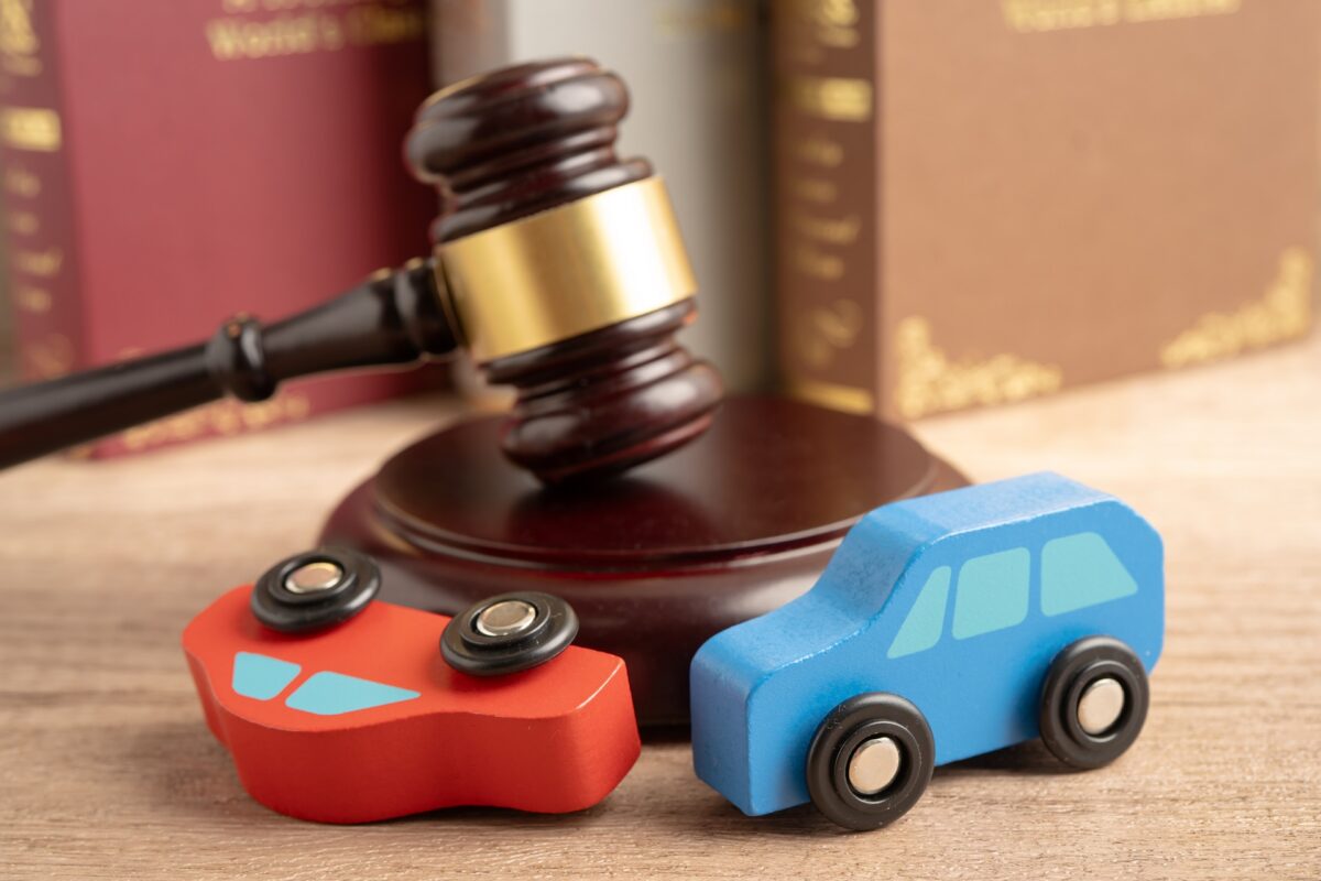Red and blue model cars sit in front of a gavel resting on its stand near some law books.