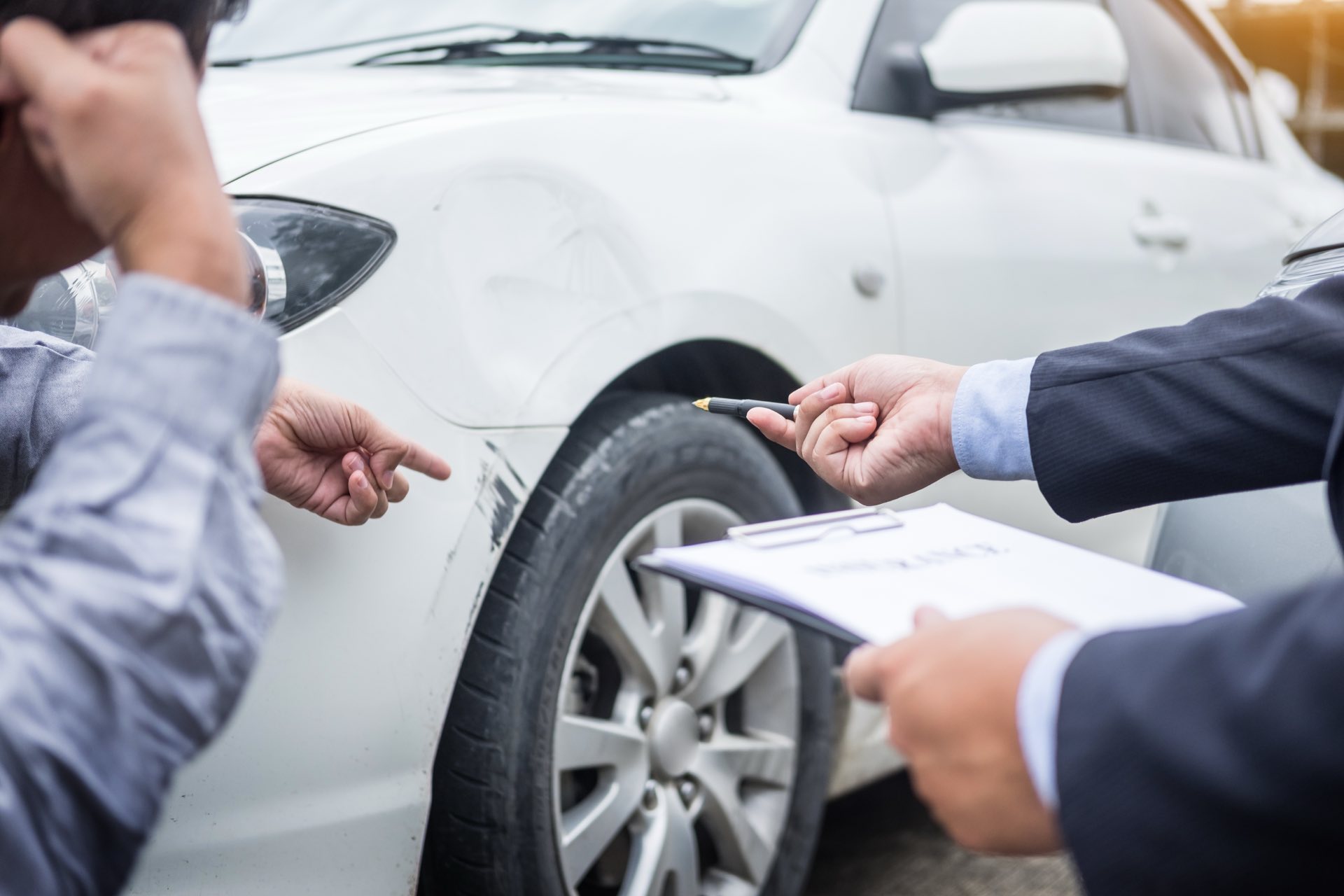 White car in an accident with a person holding a clipboard pointing to the damage